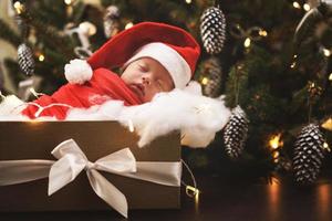 lindo bebê recém-nascido usando chapéu de papai noel está dormindo na caixa de presente de natal foto