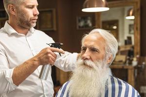 cabeleireiro fazendo corte de cabelo elegante para um velho bonito foto