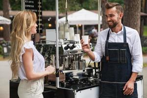 homem barista dando xícara de café para cliente mulher foto