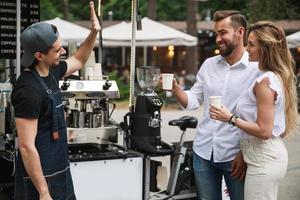 homem barista vendendo café para jovem casal na cafeteria móvel foto