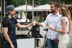 homem barista vendendo café para jovem casal na cafeteria móvel foto