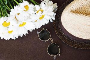 elegante chapéu de palha, óculos escuros e flores de camomila. foto