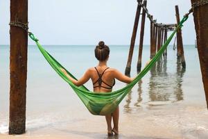 mulher está relaxando na rede pendurada em vigas velhas do cais quebrado foto