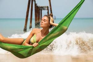 mulher está relaxando na rede pendurada em vigas velhas do cais quebrado foto