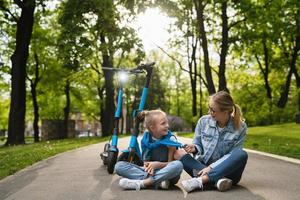 mãe e filha sentadas em uma estrada após passeio de patinetes elétricos foto