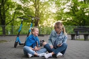 mãe e filha sentadas em uma estrada após passeio de patinetes elétricos foto