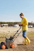 Aldeão de mulher está usando máquina de aerador para escarificação e aeração de gramado ou prado foto