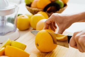 mãos femininas com faca cortando fruta laranja para suco fresco caseiro foto
