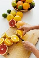 mãos femininas com faca cortando frutas cítricas na tábua para suco fresco caseiro foto