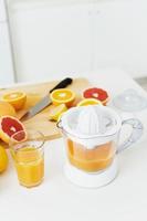 copo de suco de laranja, espremedor de frutas cítricas e várias frutas cítricas na mesa da cozinha foto