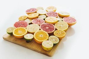 frutas cítricas fatiadas, como toranja, laranja, limão e limão na tábua contra fundo branco foto