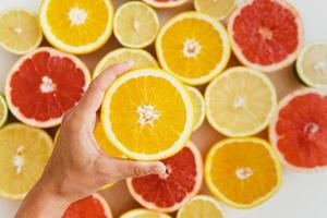 mão feminina com metade de laranja contra fundo de frutas cítricas foto