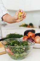 mãos femininas apertando e adicionando suco de limão à salada vegetariana foto