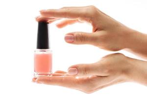 mãos femininas com linda manicure francesa segurando garrafa de esmalte rosa contra fundo branco foto