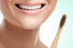 boca feminina com dentes brancos e escova de dentes de bambu foto