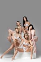 grupo de diferentes mulheres vestindo lingerie branca em fundo cinza. foto