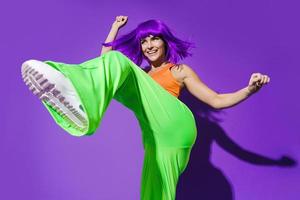 dançarina despreocupada vestindo roupas esportivas coloridas se divertindo contra o fundo roxo foto