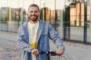 jovem alegre montando sua e-scooter na rua da cidade foto