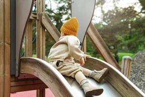 menino bonito sentado no escorregador do playground no parque público foto