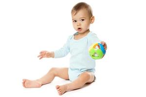 menino de macacão sentado e brincando com um brinquedo de plástico. foto