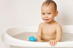 menino sorridente tomando banho com brinquedos de borracha. foto