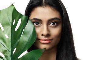 linda mulher indiana com uma pele lisa segurando folha tropical verde foto