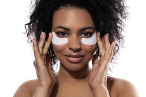 linda mulher negra com uma pele lisa aplicando manchas adesivas sob os olhos para olheiras foto