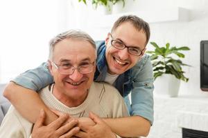 o velho em uma cadeira de rodas e seu filho. um homem abraça seu pai idoso. eles estão felizes e sorrindo foto