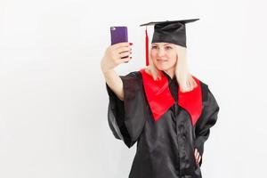 estudante feliz e animada graduada está de pé no salão da universidade em manto com diploma na mão, sorrindo e olhando para a câmera foto