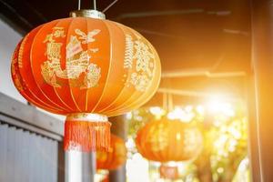 closeup lindas lanternas vermelhas de decoração chinesa penduradas no teto antigo do santuário com fundo embaçado e reflexo do sol. letras chinesas na lanterna é um elogio de bênção da fortuna média em inglês. foto