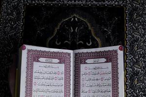 al-quran que está acima do tapete de oração com fundo preto foto