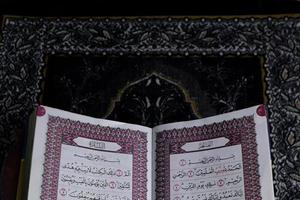 al-quran que está acima do tapete de oração com fundo preto foto