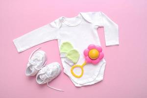 body para recém-nascido, botas, chocalho, luvas em um fundo rosa foto