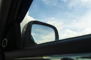 vista do foco interno do carro no lado do espelho do carro. vista para o céu azul e nuvens brancas. foto