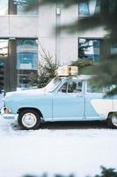 carro azul claro vintage decorado com árvore de natal natural e caixas com presentes na rua de inverno foto