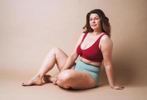 jovem que ama a si mesma plus size em cueca sentada sobre fundo bege, amor corporal foto