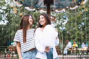 mulheres jovens com amigos de cabelo comprido com algodão doce nas mãos se divertindo no parque de diversões foto