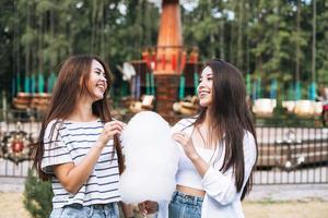 mulheres jovens com amigos de cabelo comprido com algodão doce nas mãos se divertindo no parque de diversões foto