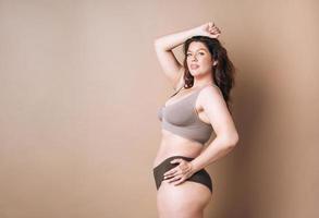 retrato de mulher amorosa plus size em cueca em fundo bege, amor corporal foto