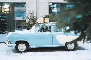 carro azul claro vintage decorado com árvore de natal natural e caixas com presentes na rua de inverno foto