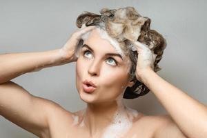 jovem mulher bonita está lavando o cabelo com um shampoo foto