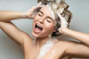 jovem mulher bonita cantando e lavando o cabelo com xampu foto