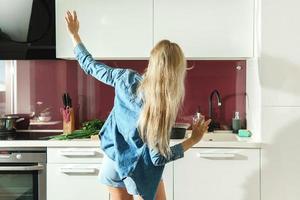mulher atraente dançando na cozinha enquanto cozinha durante a manhã ensolarada foto