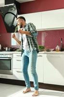 homem bonito dançando e cantando na cozinha enquanto cozinha durante a manhã ensolarada foto