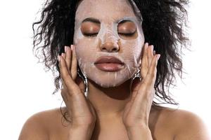 linda mulher negra com uma pele lisa aplicando máscara de folha facial foto