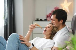 casal preguiçoso e feliz comendo pizza na cama foto