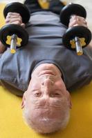 homem idoso exercitando com halteres durante seu treino no ginásio em casa foto