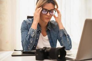 fotógrafo de mulher sofrendo de dor de cabeça em seu local de trabalho em casa foto