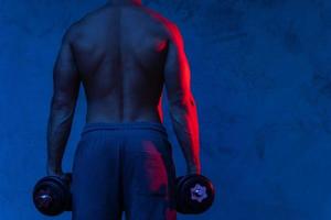 homem musculoso fisiculturista exercitando com halteres em luz neon colorida foto