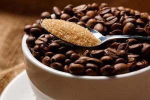 xícara cheia de grãos de café e colher com açúcar mascavo foto